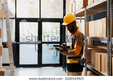 African american storehouse employee checking scanned product in digital tablet. Man industrial warehouse manager holding barcode scanner and using stock inventory software app