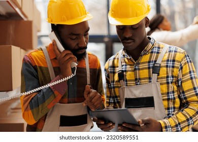 African american storehouse employees coordinating delivery schedule with logistics manager on landline telephone. Warehouse operator talking on phone and looking at digital tablet screen - Powered by Shutterstock