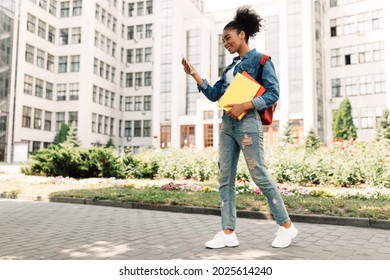 African American Student Girl Using Smartphone Browsing Internet Standing Outdoors Near College Building. Black Female Teen Texting Via Smartphone. Educational Mobile Application. Full Length