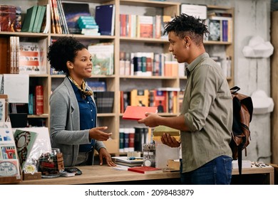 African American student talking to librarian while returning book at the library. 