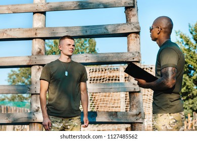 african american tactical instructor with notepad and young soldier in military uniform on range - Shutterstock ID 1127485562