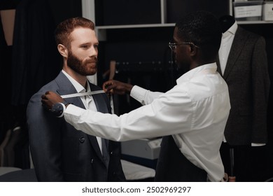 African American tailor measures tailored suit, discusses with client size in luxury designer atelier. - Powered by Shutterstock