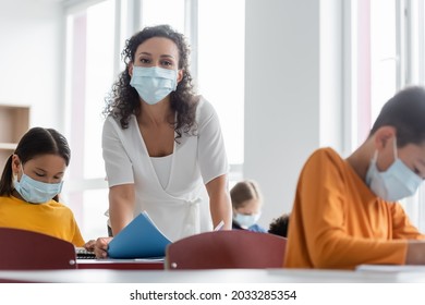 African American Teacher In Medical Mask Near Multiethnic Kids In Classroom