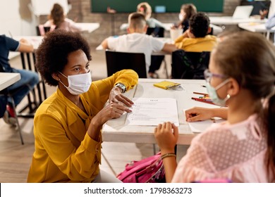 African American teacher and schoolgirl wearing protective face masks while discussing about test results on a class at the school. 