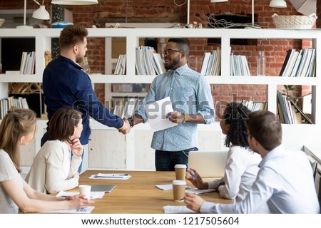 African American team leader or boss handshake Caucasian employee congratulating with work success, black manager shake hand of male worker greeting with high results and personal achievements