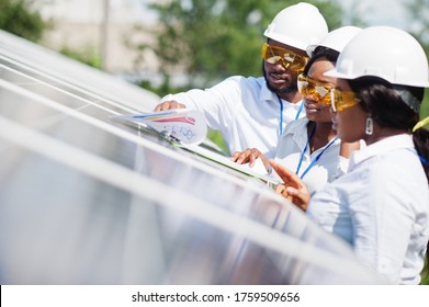 African American Technician Checks The Maintenance Of The Solar Panels. Group Of Three Black Engineers Meeting At Solar Station.