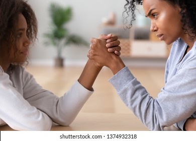 African American teen daughter and mother arm wrestling family conflict, disagreement and confrontation, teenager girl and angry mum having fight, holding hands with serious faces, close up - Powered by Shutterstock