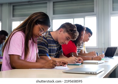 African american teen high school student writing in class. Group of college students taking notes in class.