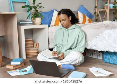 African American Teen School Girl Distant School Or College Student Virtual Remote E Learning Using Laptop In Bedroom Taking Notes. Distance Education Classes, Studying Online At Home Concept.