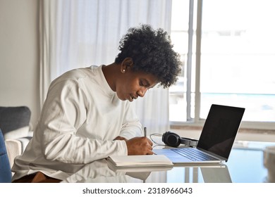 African American teen student elearning, writing notes at home. Serious teenage boy using computer learning online virtual class, taking english web course writing notes sitting at home table. - Powered by Shutterstock