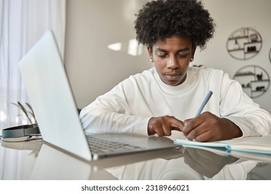 African American teenage boy student using computer watching webinar, learning english online virtual elearning class, taking english web course writing notes sitting at home table.