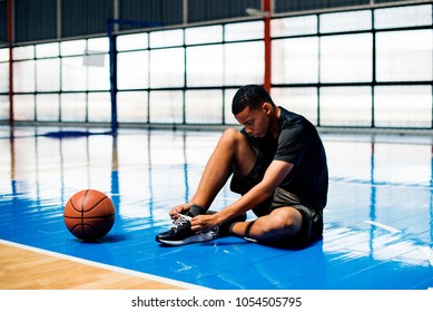 African American teenage boy tying his shoe laces on a basketball court - Powered by Shutterstock