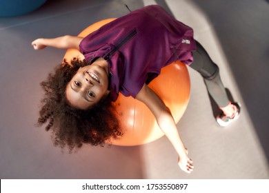 African American Teenage Girl Smiling At Camera While Working Out With Exercise Ball In Gym. Sport, Healthy Lifestyle, Physical Education Concept. Horizontal Shot