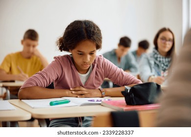 African American teenage girl studying from a book during a class at high school. - Powered by Shutterstock