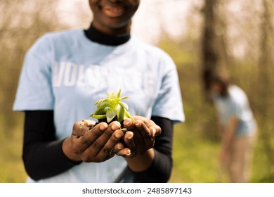 African american teenager advocating ecology by holding a small plant, growing seedlings in organic soil for future generations. Young girl preserving natural environment in the forest. - Powered by Shutterstock