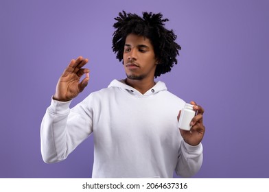 African American Teenager Holding Jar And Pill Over Violet Studio Background. Funky Black Adolescent Taking Medication For Cold Or Flu, Painkiller Or Vitamin. Health Care, Treatment Of Coronavirus