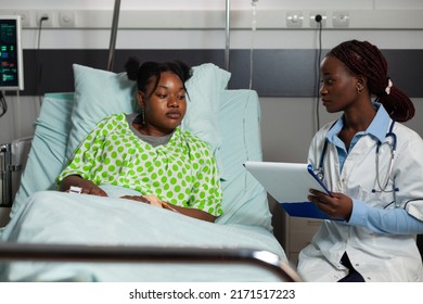 African American Therapist Doctor Sitting Beside Sick Patient Asking Medical Question During Clinical Consultation In Hospital Ward. Specialist Woman Prescribing Healthcare Treatment. Medicine Service