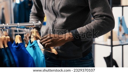 African american thief shoplifting trendy clothes in modern boutique, being caught by asian security guard. Bodyguard asking robber to return stylish merchandise or will call the police