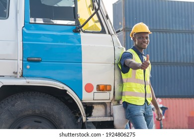 African American Transportation Factory Truck Driver With Helmet And Safety Vest Is Standing, Smile And Thumb Up At Heavy Lorry Of Container Yard In Logistic Construction Port. Black Skin Worker.