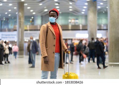 African American traveler man with yellow suitcase stands in airport terminal, wear face medical mask to protect yourself from contact with flu virus. Second wave Covid-19, coronavirus. New normal.