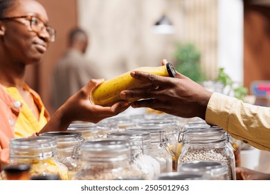 African American vendor sells organic, locally sourced groceries in sustainable supermarket. Female customer receives plastic-free pantry staples and fresh produce from the shopkeeper. Close-up shot. - Powered by Shutterstock