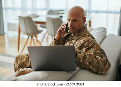 African American Veteran Using Laptop While Talking On Mobile Phone In The Living Room. 