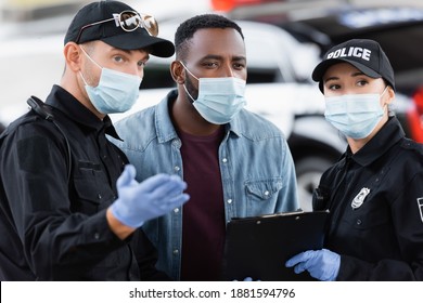 African American Victim In Medical Mask Standing Near Police Officers With Clipboard On Urban Street