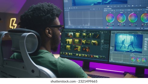 African American video editor makes color grading, works at home office. Action movie footage and program interface on multi-monitor computer and big digital screen. Concept of film post production. - Shutterstock ID 2321499665