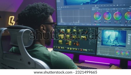 African American video editor makes color grading, works at home office. Action movie footage and program interface on multi-monitor computer and big digital screen. Concept of film post production.