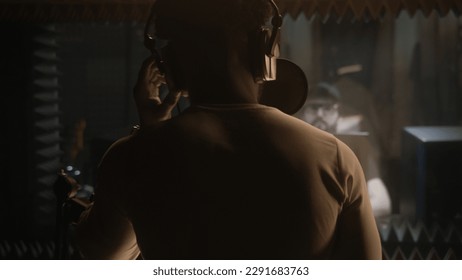 African American vocalist sings composition into microphone in soundproof room. Experienced audio engineer or producer works with singer in sound recording studio. Music production concept. Back view. - Powered by Shutterstock