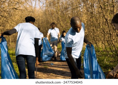 African american volunteers team working to clean the forest from trash, combat forest pollution to protect the natural habitat. Young man and woman activists collecting garbage. - Powered by Shutterstock