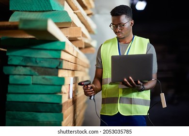 African American Warehouse Worker Using Laptop And Scanning Labels At Lumber Storage Compartment.