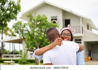African American wife hugging her husband in front of the house they just move in while holding key for housing, relocation and new family concept
