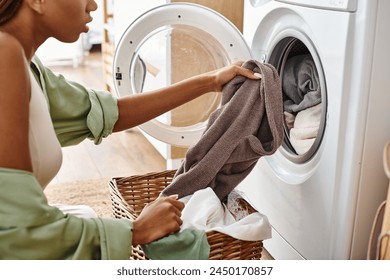 African American woman with afro braids putting a cloth into a dryer in a bathroom during laundry time. - Powered by Shutterstock