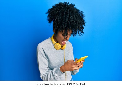 African American Woman With Afro Hair Using Smartphone Typing Message Angry And Mad Screaming Frustrated And Furious, Shouting With Anger. Rage And Aggressive Concept. 