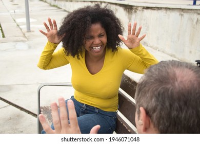 African American Woman With Afro Hair And Yellow T-shirt Speaking Sing Language Sitting On A Wooden Bench.