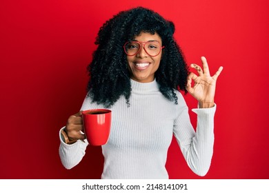 African american woman with afro hair holding coffee doing ok sign with fingers, smiling friendly gesturing excellent symbol  - Powered by Shutterstock