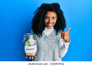 African American Woman With Afro Hair Holding Savings Jar With South African Rands Money Smiling Happy And Positive, Thumb Up Doing Excellent And Approval Sign 