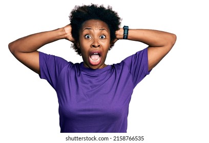 African american woman with afro hair wearing casual purple t shirt crazy and scared with hands on head, afraid and surprised of shock with open mouth  - Powered by Shutterstock