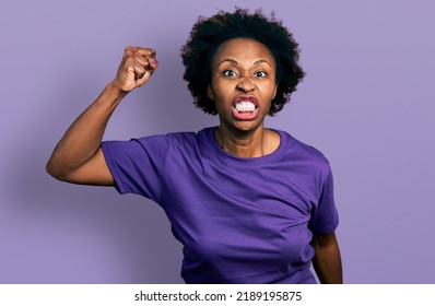 African american woman with afro hair wearing casual purple t shirt angry and mad raising fist frustrated and furious while shouting with anger. rage and aggressive concept.  - Shutterstock ID 2189195875