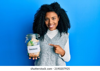 African American Woman With Afro Hair Holding Savings Jar With South African Rands Money Smiling Happy Pointing With Hand And Finger 