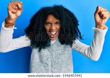 African american woman with afro hair wearing casual winter sweater angry and mad raising fists frustrated and furious while shouting with anger. rage and aggressive concept. 