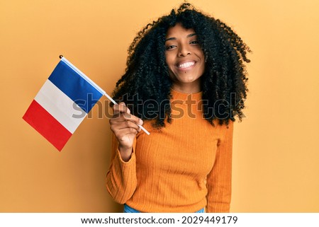 African american woman with afro hair holding france flag looking positive and happy standing and smiling with a confident smile showing teeth 