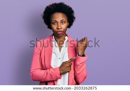 African american woman with afro hair wearing business jacket in hurry pointing to watch time, impatience, looking at the camera with relaxed expression 