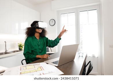 An African American woman with afro hairstyle is presenting home projects via virtual reality using laptop with drafts working at home - Powered by Shutterstock