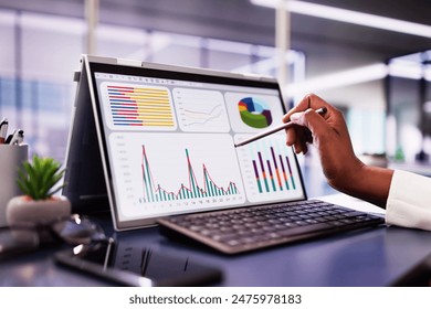 African American woman analyzing financial data on laptop screen in hybrid office setting for digital entrepreneurship KPI dashboard.