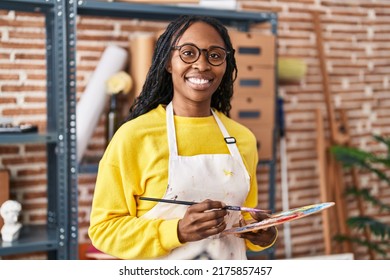 African american woman artist smiling confident holding paintbrush and palette at art studio