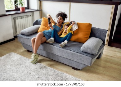 African american woman, baby sitter and caucasian cute little girl having fun together, playing video games, sitting on the couch. Children education, leisure activities, babysitting concept