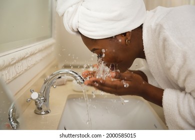 African american woman in bathroom with towel on head, standing at basin washing face. health, beauty and wellbeing, spending quality time at home. - Powered by Shutterstock