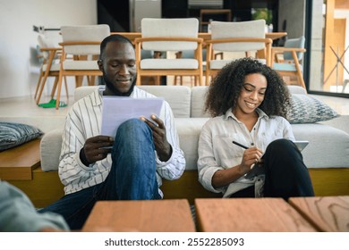 African American woman and Black man engage in work dialogue, analyzing documents in a cozy modern office lounge, their casual business attire suggesting an informal, collaborative environment. - Powered by Shutterstock